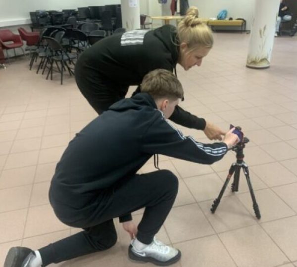 Noormees ja naine seadistavad põrandal statiivile kinnitatud nutitelefoni, valmistudes filmimiseks.